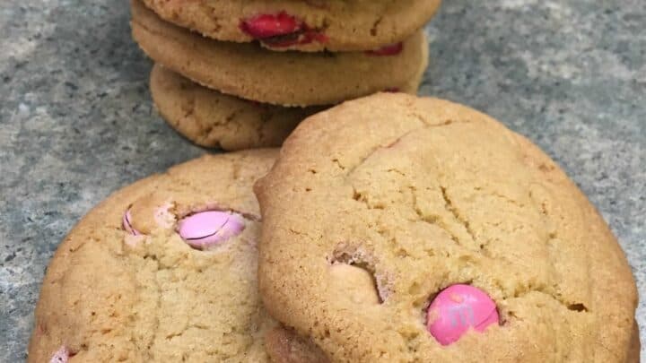 Pink and white M&M cookies stacked on a counter