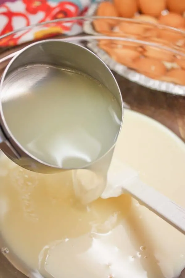 pouring lemon juice into a large mixing bowl with sweetened condensed milk.