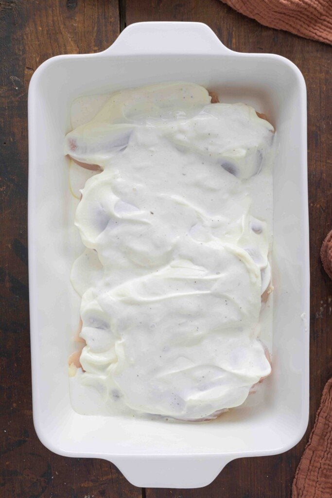 Ranch dressing on top of chicken breasts in a baking dish.