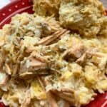 Slow cooker pork chops and rice with cheese on a red plate with two biscuits.