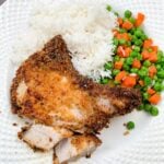 Breaded air fryer pork chops on a white plate with white rice and mixed veggies.