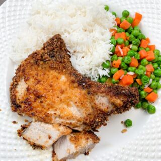 Breaded air fryer pork chops on a white plate with white rice and mixed veggies.