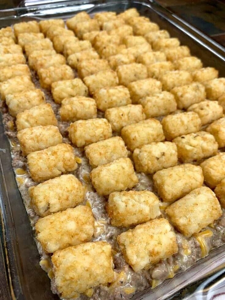 A casserole dish filled with rows of golden-brown tater tots arranged neatly on top of a creamy, baked mixture, likely containing ground meat and sauce—the best Tater tot casserole recipe.