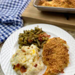 Panko chicken breast on a white plate with green beans and potatoes.