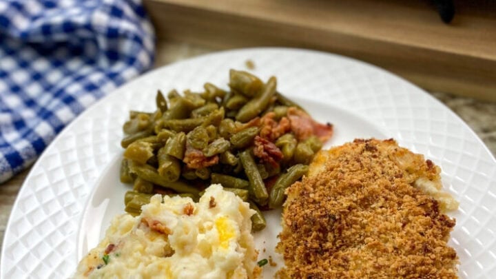 Panko chicken breast on a white plate with green beans and potatoes.