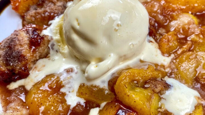 Peach cobbler on a round plate with ice cream on top.