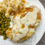 Baked chicken and ranch dinner on a white plate with peas and potatoes.