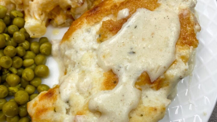 Baked chicken and ranch dinner on a white plate with peas and potatoes.