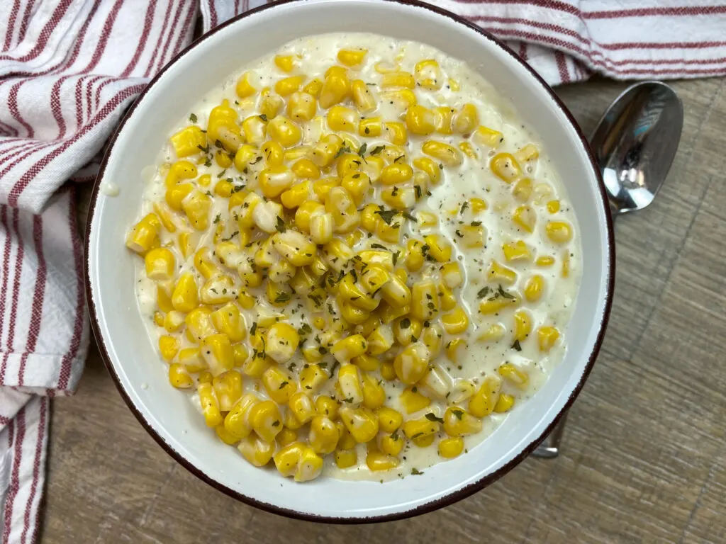 Creamed corn in a white bowl with a red and white towel on the counter.