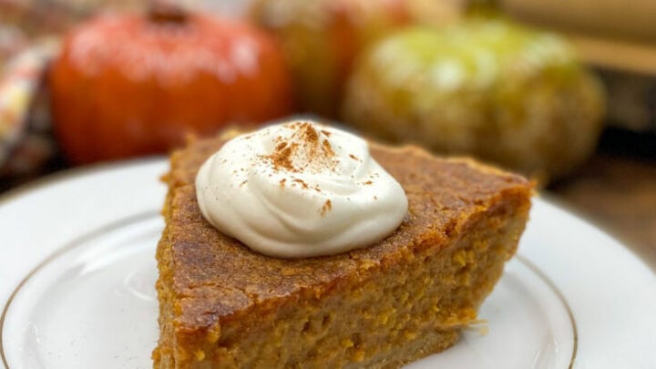 A slice of pie on a white plate with ceramic pumpkins in the background.