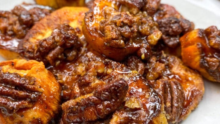 Glazed sweet potatoes with pecans on a white plate.