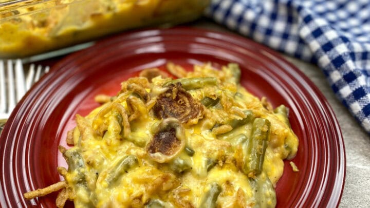 Holiday green bean casserole on a red plate with cheese and onions.