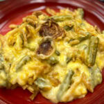 Holiday green bean casserole on a red plate with cheese and onions.