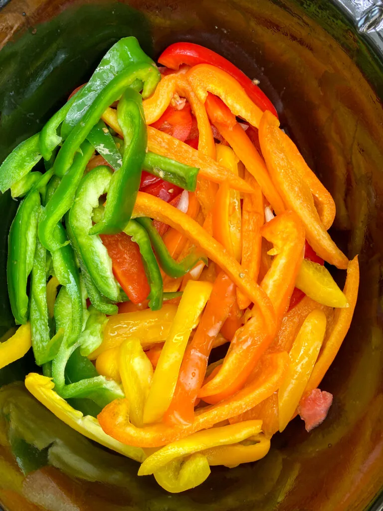 Green, red, orange, and yellow bell peppers sliced in a slow cooker.