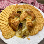 Baked brie on a white plate with crackers.