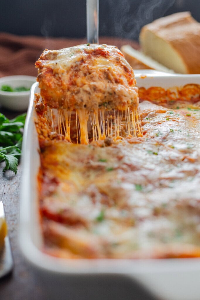 A slice of cooked lasagna being lifted out of a pan. There is a lot of stringy cheese.