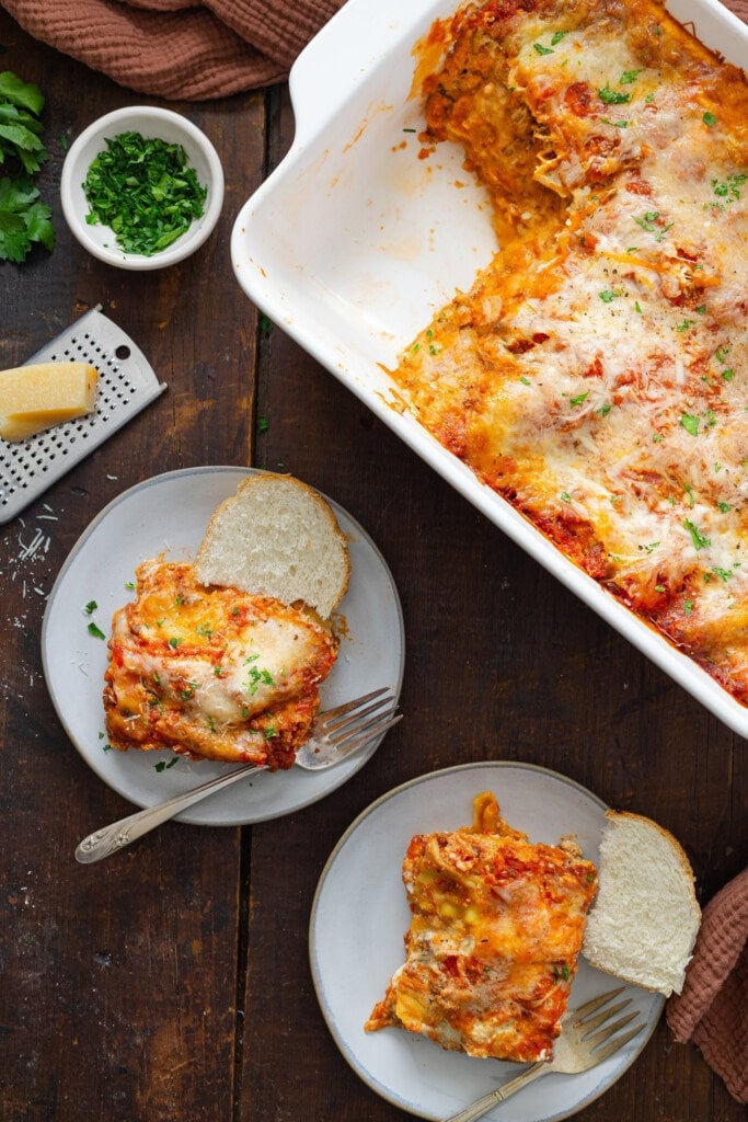 A slice of lasagna on a plate next to a casserole dish with lasagna.