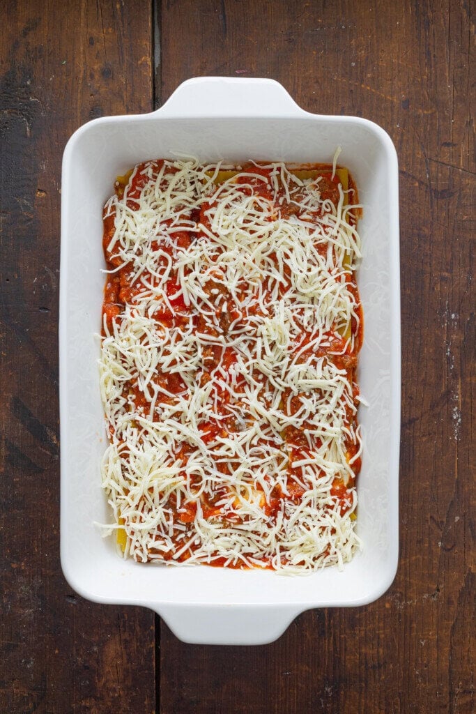 Layering lasagna in a casserole dish. There is shredded mozzarella on top.
