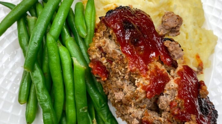 Classic meatloaf on a white plate with potatoes and green beans.