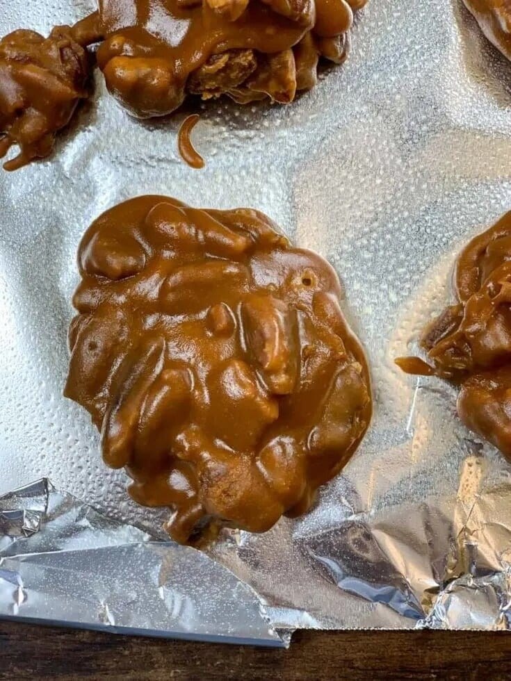 A close-up of a praline candy cluster from an easy praline pecans recipe, featuring a glossy caramel coating and visible nuts, resting on crinkled aluminum foil—classic Southern candy at its finest.