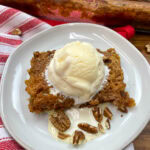 An ice cream scoop on top of pecan pie cake on a white plate.