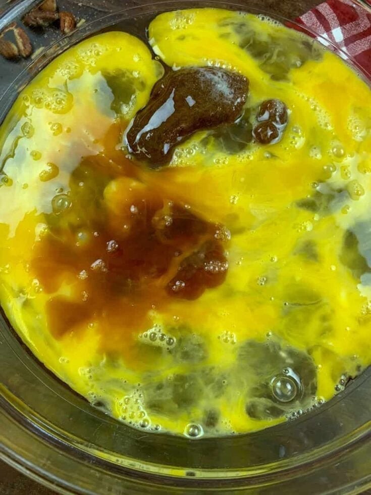 A close-up of a glass bowl containing cracked eggs, vanilla extract, and brown sugar, ready to be mixed for this Easy Pecan Pie Cobbler Recipe.