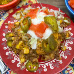 Mexican casserole on a red plate with jalapenos, tomatoes, and corn