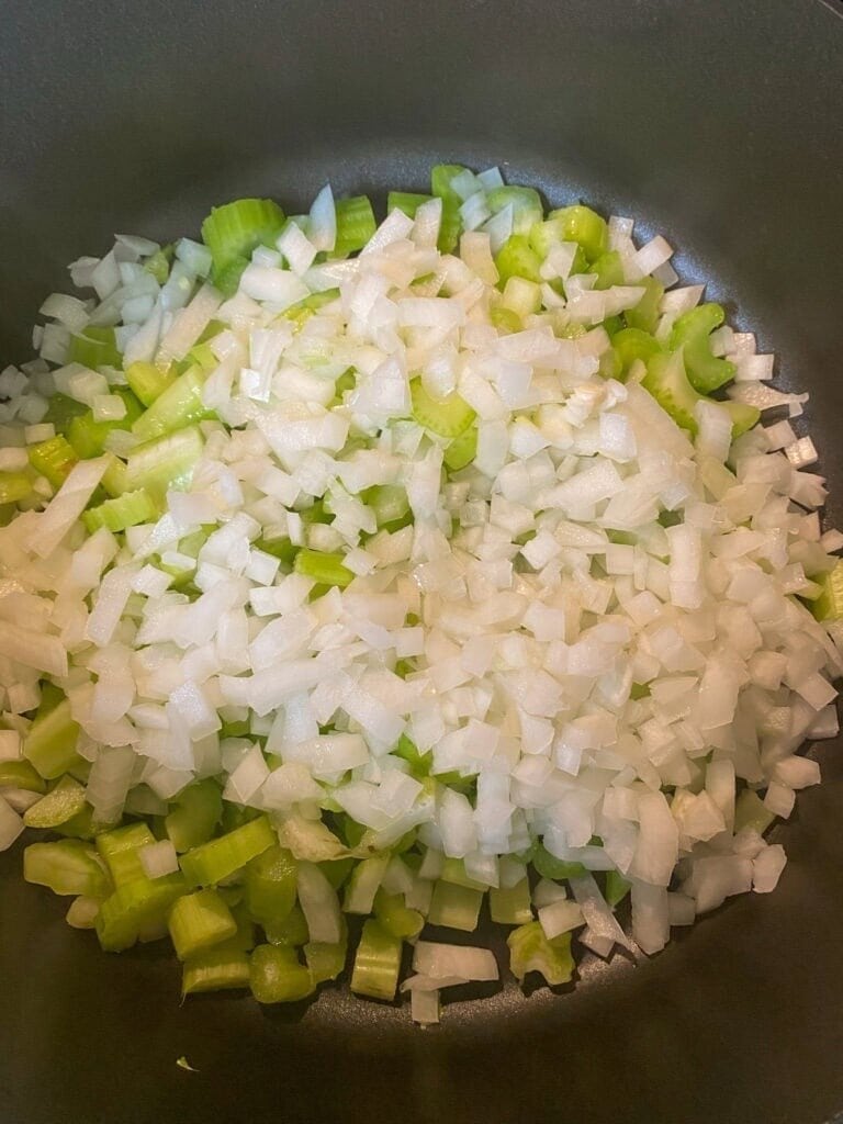 Chopped white onions and sliced celery pieces in a pot, ready to be cooked for a classic Jiffy Cornbread Dressing Recipe.