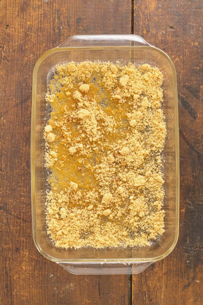 A glass baking dish filled with a crumbly, golden-brown sugar for a Pineapple Upside Down Cake Recipe With Cake Mix, sits on a rustic wooden surface.