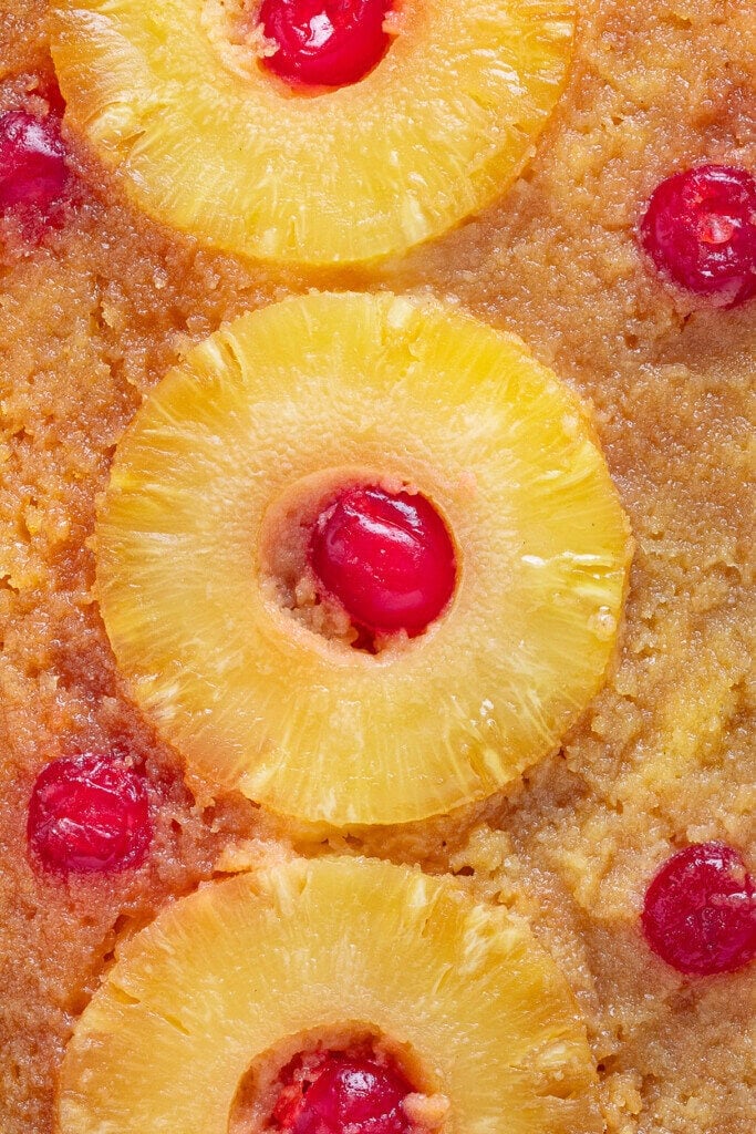 Close-up of a Pineapple Upside Down Cake Recipe With Cake Mix, featuring rings of pineapple with red maraschino cherries in the centers and a golden-brown, caramelized cake surface.