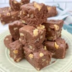 Pieces of million dollar fudge stacked on top of each other on an off-white plate.