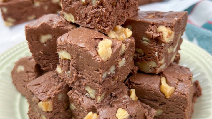 Pieces of million dollar fudge stacked on top of each other on an off-white plate.
