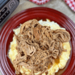 Slow cooker tenderloin on a red plate on top of mashed potatoes.