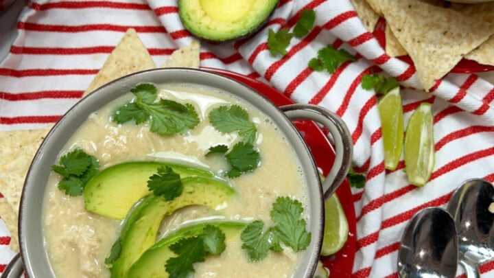 White chicken chili in a brown bowl with sliced avocado and cilantro.