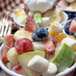 Fruit salad in small bowls with whipped cream on top.