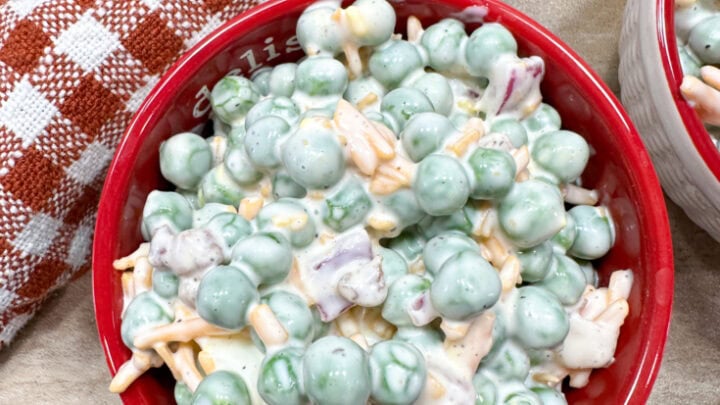 English pea salad in a red bowl. There is a large mixing bowl behind the bowl.