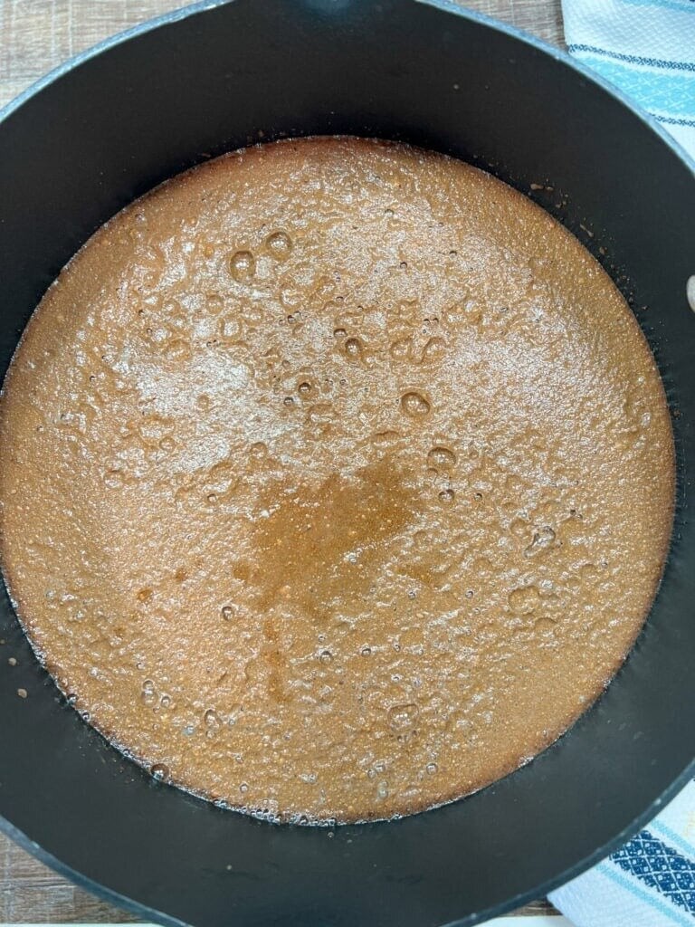 A close-up of pie ingredients bubbling in a black saucepan on a wooden surface, with a blue and white striped towel partially visible—an essential step for any delicious Homemade Chocolate Cream Pie Recipe.