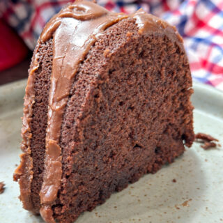 A slice of chocolate pound cake. There is chocolate frosting on top of the slice and sliding down the side.
