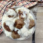 Meatballs in a bowl with mashed potatoes. They have white gravy on top.