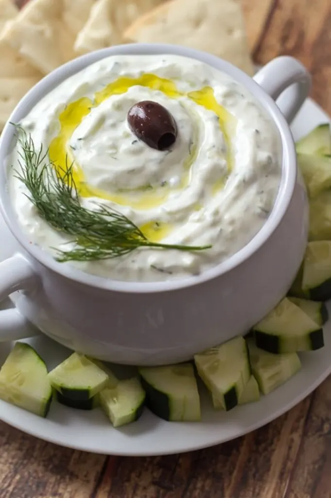 Greek tzatziki dip in a white bowl. There are some veggies around the edge of the bowl.