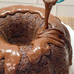 Chocolate icing being poured over a chocolate cake.