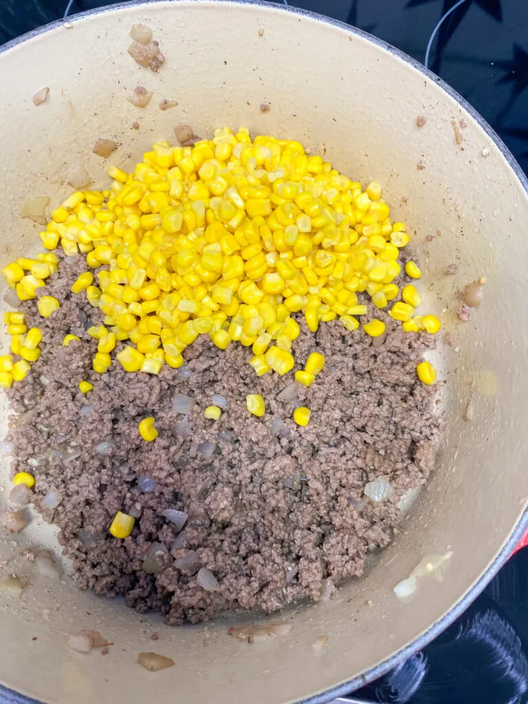 Cooked ground beef with whole kernel corn in a saucepan.