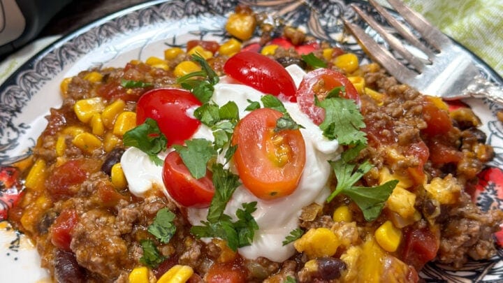 Slow cooker Mexican ground beef casserole on a red, black, and white plate. The casserole is topped with cilantro and grape tomatoes.