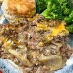 Ground beef and potato casserole on a plate with some broccoli and a biscuit.