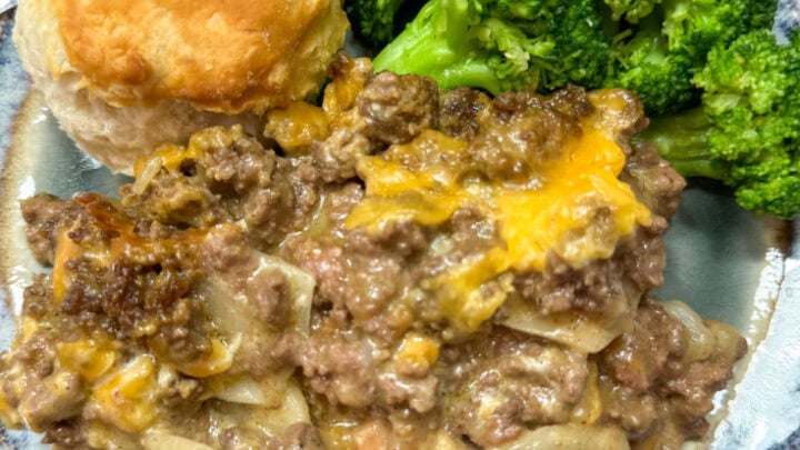 Ground beef and potato casserole on a plate with some broccoli and a biscuit.