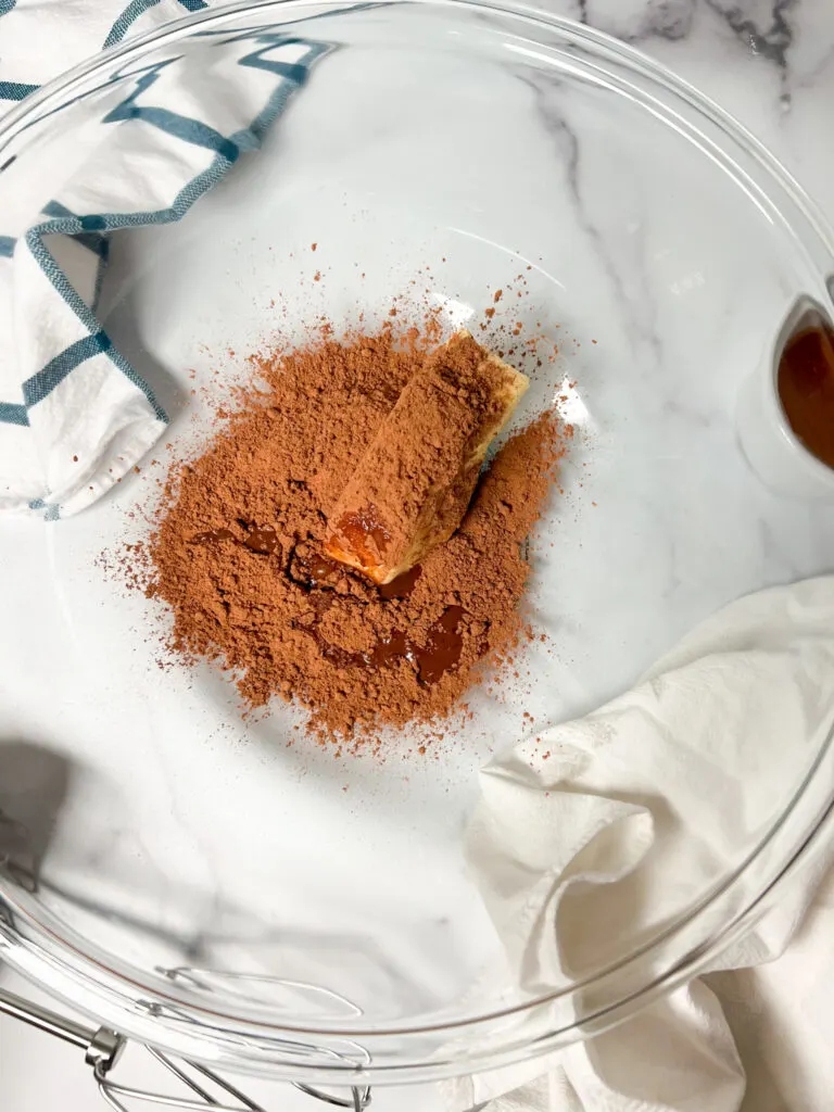 Butter, cocoa, and vanilla extract in a clear glass mixing bowl.