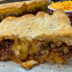 Sloppy joe crescent roll with cheese on a white plate. The plate is on top of a wooden plate.