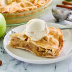 A slice of apple pie on a white plate with a scoop of ice cream on top.