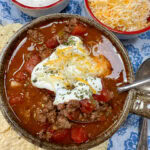 Beanless chili on the counter with sour cream and shredded cheese on top.
