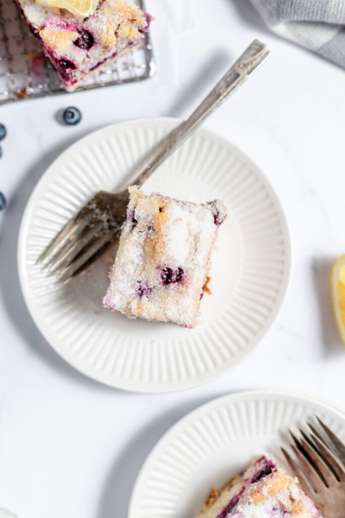 Blueberry coffee cake on a white plate. There's other slices near the plate.